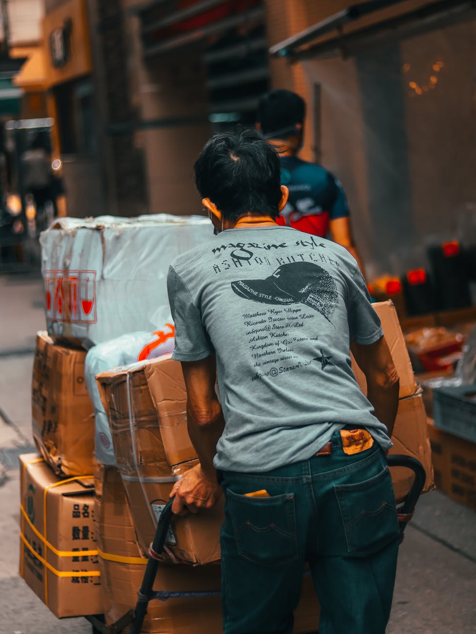 unrecognizable male worker carrying cart with heavy carton boxes